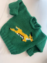 Green and gold hand-knitted baby rugby jersey with animal design, flat lay