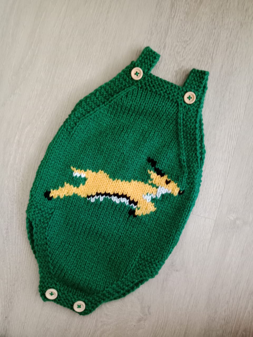 Green and gold hand-knitted baby romper with animal design and wooden buttons
