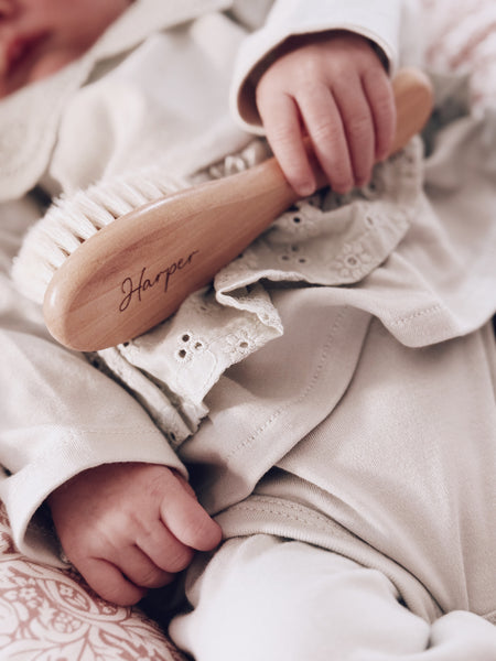 Baby holding a personalised wooden hairbrush with name engraving